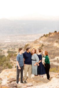 family of five with a little white puppy posing for family photos at palmer park in Colorado Springs overlooking Pikes Peak