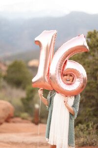 teenage girl photoshoot at garden of the gods in Colorado Springs, smiling holding balloons with the number 16